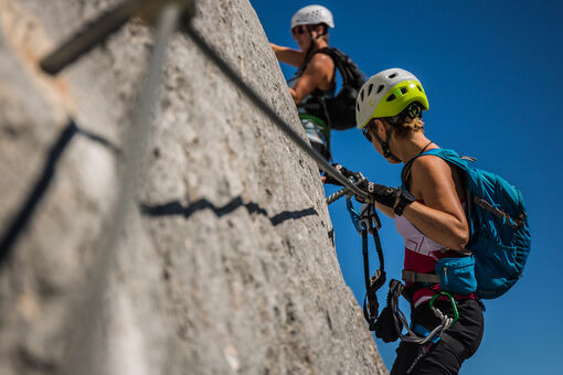 Zwei Frauen klettern an einem im Rofangebirge liegenden Klettersteig bei tollem Wetter und atemberaubendem Ausblick.