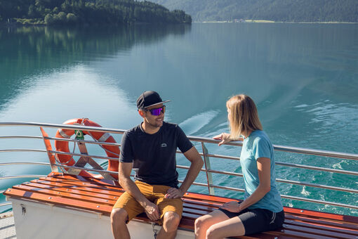 A couple enjoying a boat trip with the Achenseeschifffahrt, enjoying the water and the beautiful natural surroundings.
