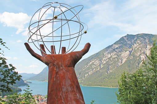 Eine Skulptur einer Hand die einen eisernen durchsichtigen Planeten auf dem Besinnungsweg am in Pertisau hält.