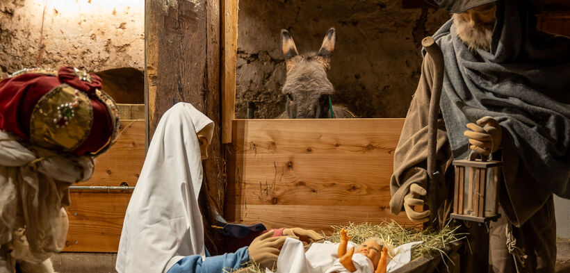 The picture shows a nativity scene in the history museum Sixenhof in Achenkirch with figures of Mary, Joseph and a newborn baby in straw. A donkey can be seen in the background.