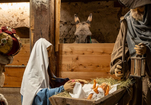 Tiroler Bergweihnacht im Sixenhof Das Bild zeigt eine Weihnachtskrippe im Heimatmuseum Sixenhof in Achenkirch mit Figuren von Maria, Josef und einem Neugeborenen im Stroh. Im Hintergrund ist ein Esel zu sehen.