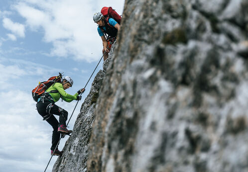 Klettersteige am Achensee Ein Mann und eine Frau auf einem Klettersteig im Rofangebirge bei wenig bewölktem Himmel.