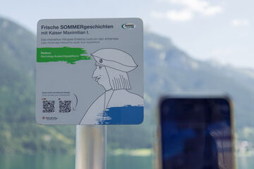 Ein Informationsschild am Aussichtspunkt Hochsteg am Achensee. Es bewirbt eine interaktive Hörspiel-Tour mit Kaiser Maximilian I. und enthält Anweisungen zum Scannen eines QR-Codes, um mehr über die Geschichte und die Umgebung zu erfahren.