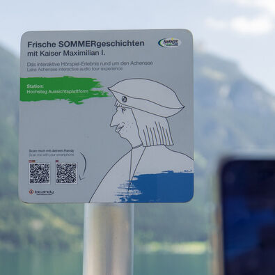 Ein Informationsschild am Aussichtspunkt Hochsteg am Achensee. Es bewirbt eine interaktive Hörspiel-Tour mit Kaiser Maximilian I. und enthält Anweisungen zum Scannen eines QR-Codes, um mehr über die Geschichte und die Umgebung zu erfahren.
