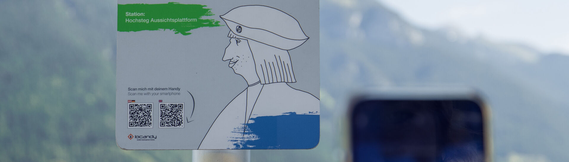 Ein Informationsschild am Aussichtspunkt Hochsteg am Achensee. Es bewirbt eine interaktive Hörspiel-Tour mit Kaiser Maximilian I. und enthält Anweisungen zum Scannen eines QR-Codes, um mehr über die Geschichte und die Umgebung zu erfahren.