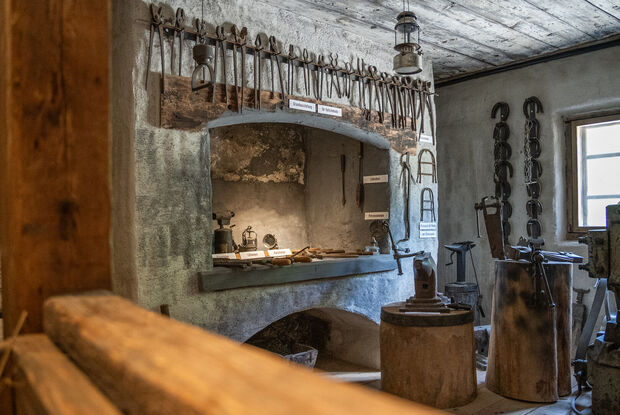 Heimatmuseum Sixenhof in Achenkirch Das Bild zeigt eine historische Schmiede im Heimatmuseum Sixenhof mit verschiedenen Werkzeugen auf einem Regalsystem.