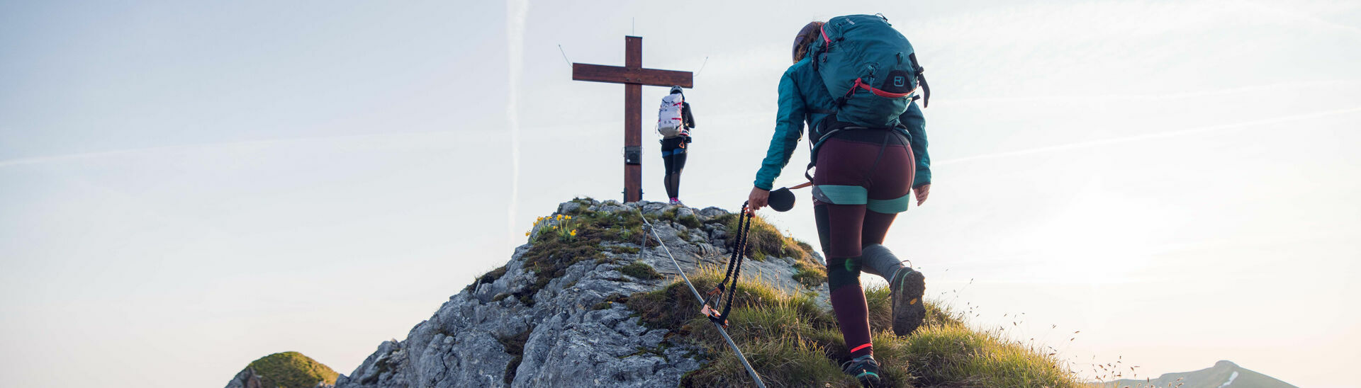 Zwei Frauen kommen gerade am Gipfelkreuz vom Rosskopf an bei schönem Wetter.