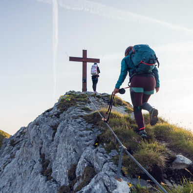Klettersteig Rosskopf Zwei Frauen kommen gerade am Gipfelkreuz vom Rosskopf an bei schönem Wetter.