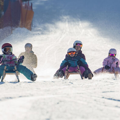 Bei herrlichem Wetter saust eine Familie die Rodelbahn in Achenkirch hinunter. Die Landschaft ist schneebedeckt.