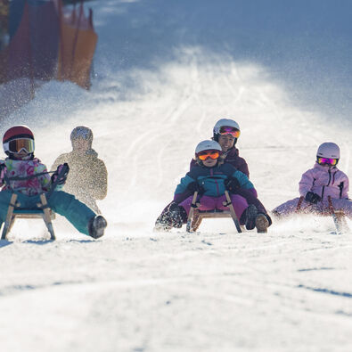 Bei herrlichem Wetter saust eine Familie die Rodelbahn in Achenkirch hinunter. Die Landschaft ist schneebedeckt.