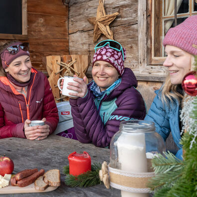 A group of friends enjoy tea and a snack on the terrace of a mountain hut.
