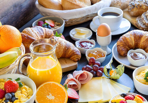 Seerundfahrt & Brunch Reich gedeckter Frühstückstisch mit Croissants, verschiedenen Brotsorten, Kaffee, Orangensaft, Ei, Rührei, Käse, Schinken, Marmelade, Müsli, frischem Obst und Butter.
