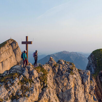 Two women who are enthusiastic about mountain sports enjoy the morning atmosphere at the Rosskopf via ferrata in the Rofan mountains.