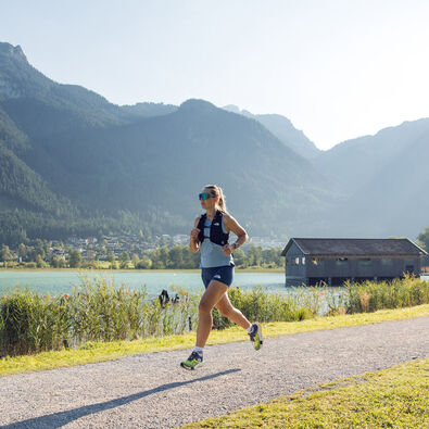 Eine Frau joggt bei schönem Wetter am Seespitz entlang, während im Hintergrund das Bootshaus zu sehen ist.