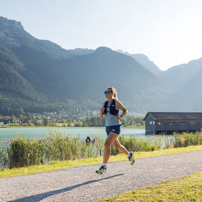 Eine Frau joggt bei schönem Wetter am Seespitz entlang, während im Hintergrund das Bootshaus zu sehen ist.