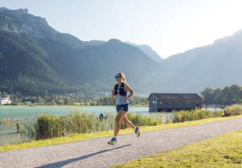 Eine Frau joggt bei schönem Wetter am Seespitz entlang, während im Hintergrund das Bootshaus zu sehen ist.