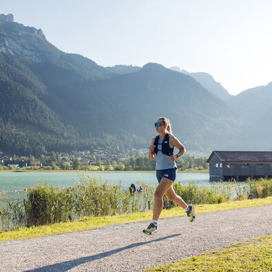 Eine Frau joggt bei schönem Wetter am Seespitz entlang, während im Hintergrund das Bootshaus zu sehen ist.