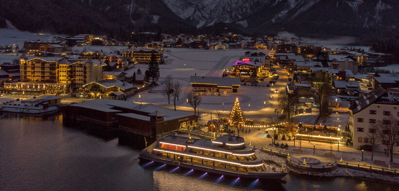 Die mit Schnee bedeckte Ortschaft Pertisau am Achensee wird in der Adventzeit wunderschön beleuchtet bei Nacht.
