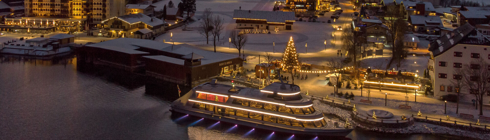 Night shot of the snow-covered village of Pertisau am Achensee in the Advent season, festooned with decorations and sparkling lights.