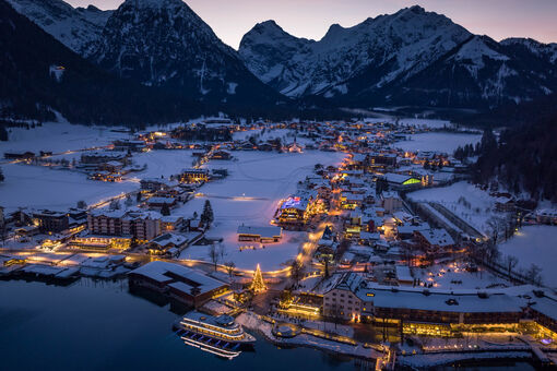 Night shot of the snow-covered village of Pertisau am Achensee in the Advent season, festooned with decorations and sparkling lights.