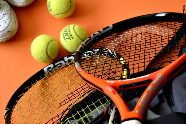 Tennis am Achensee Zwei Tennisschläger, mehrere gelbe Tennisbälle und ein weißer Tennisschuh liegen auf einem orangefarbenen Untergrund.