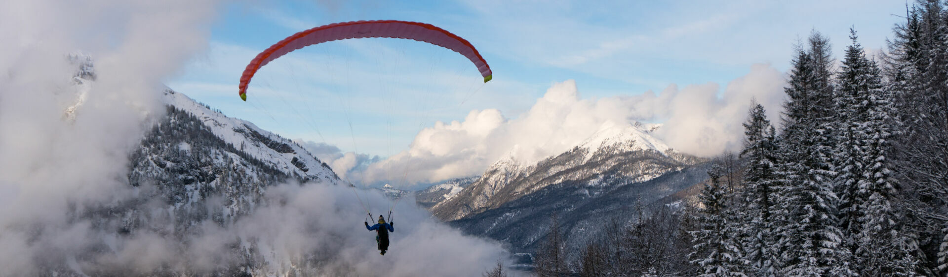 A paraglider swooping through the winter skies enjoying the view of the wintry landscape and Lake Achensee from above.