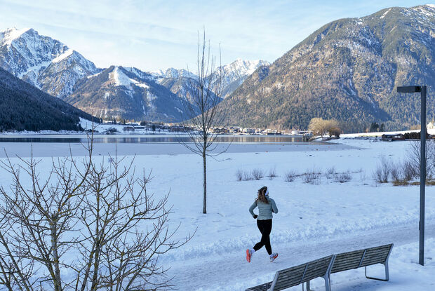 Laufen am Achensee im Winter Eine Trailrunnerin läuft im Winter am Achensee entlang und im Hintergrund sieht man das schneebedeckte Karwendel und die umliegende Berglandschaft. Neben ihr liegt der Achensee mit ruhiger Wasseroberfläche.