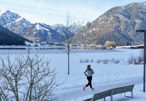 Trailrunning im Winter Eine Trailrunnerin läuft im Winter am Achensee entlang und im Hintergrund sieht man das schneebedeckte Karwendel und die umliegende Berglandschaft. Neben ihr liegt der Achensee mit ruhiger Wasseroberfläche.
