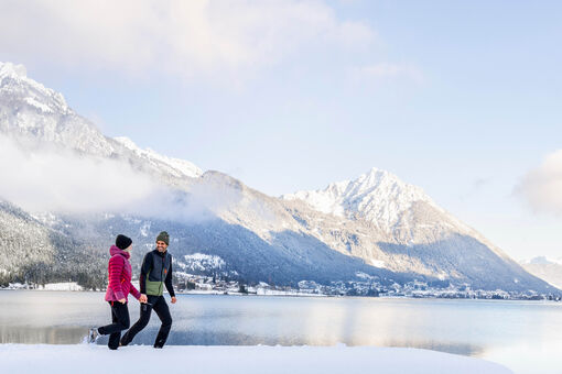 Ein Paar genießt bei einem Spaziergang die Winterlandschaft am Achensee. Im Hintergrund Maurach und das Ebner Joch.