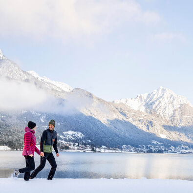 Ein Paar genießt bei einem Spaziergang die Winterlandschaft am Achensee. Im Hintergrund Maurach und das Ebner Joch.