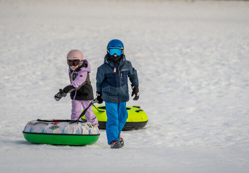 Zwei Kinder ziehen ihre Snowtubes hinter sich, nachdem sie die eigens dafür ausgewiesene Piste der Planberg- und Wiesenlifte in Pertisau hinuntergerutscht sind.