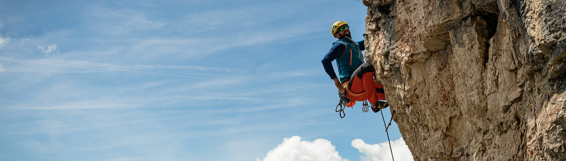 Ein Kletterer der sich gerade neu sichern möchte vor einem schönen blauen Himmel.