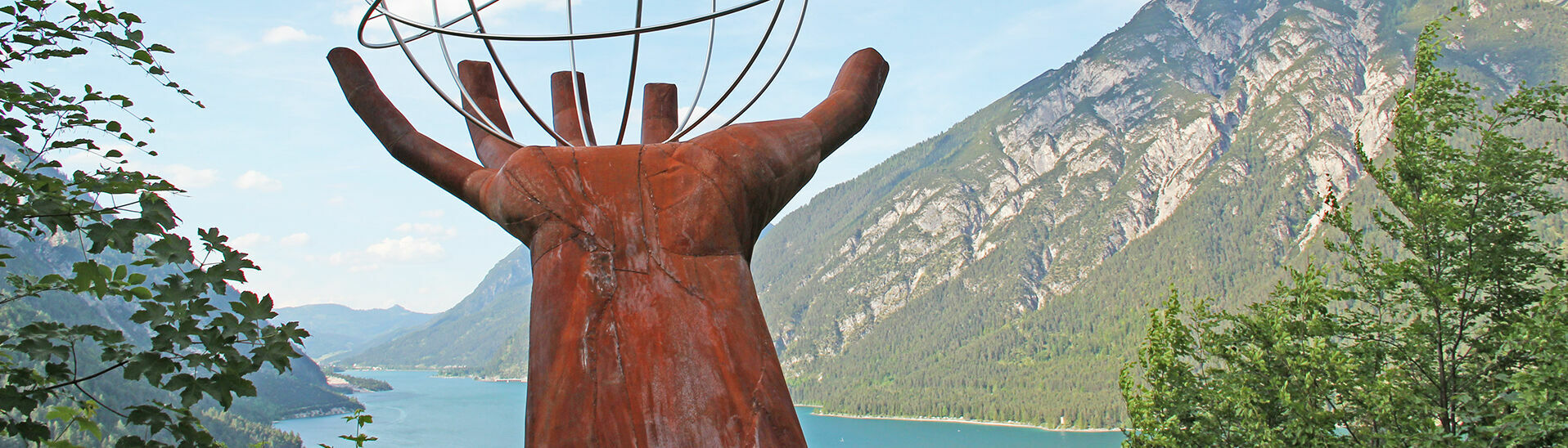 Eine Skulptur einer Hand die einen eisernen durchsichtigen Planeten auf dem Besinnungsweg am in Pertisau hält.