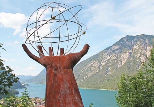 Besinnungs-Dien-Mut-Weg Eine Skulptur einer Hand die einen eisernen durchsichtigen Planeten auf dem Besinnungsweg am in Pertisau hält.