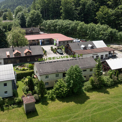 Achenseer Museums- und Erlebniswelt in Maurach An aerial view of the Achensee Museum World in Maurach surrounded by meadows and forests in summer.