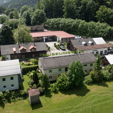 An aerial view of the Achensee Museum World in Maurach surrounded by meadows and forests in summer.