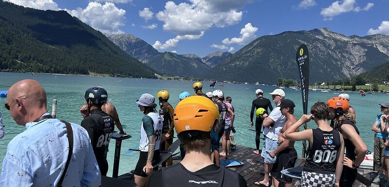 Zahlreiche Besucherinnen und Besucher nehmen an Workshops teil oder entspannen am Seeufer. Im Hintergrund sieht man das türkisblaue Wasser des Achensees und die umliegende Bergwelt.