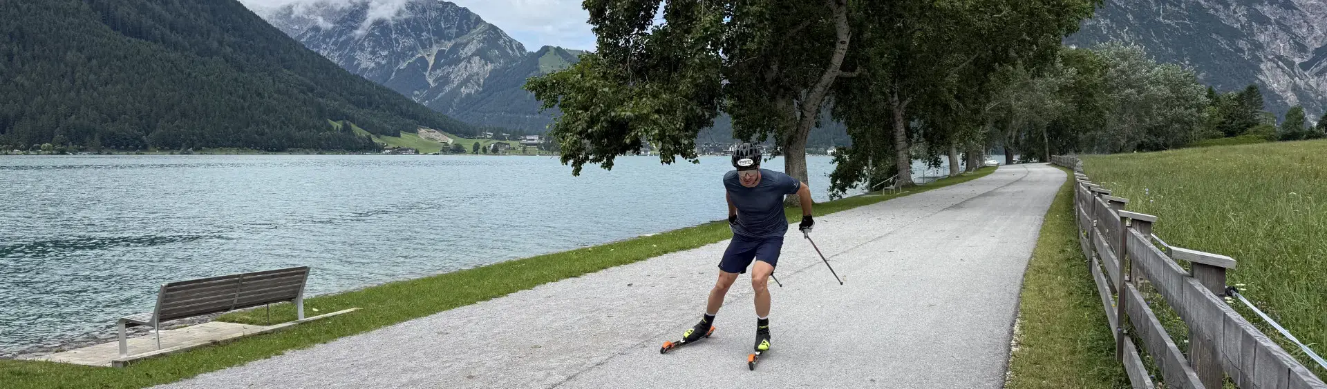 Skirollern am Achensee Ein Mann fährt mit Rollski auf einem asphaltierten Weg entlang eines Achensees. Er trägt einen Helm, Handschuhe und Sportbekleidung und nutzt Stöcke zum Antrieb.