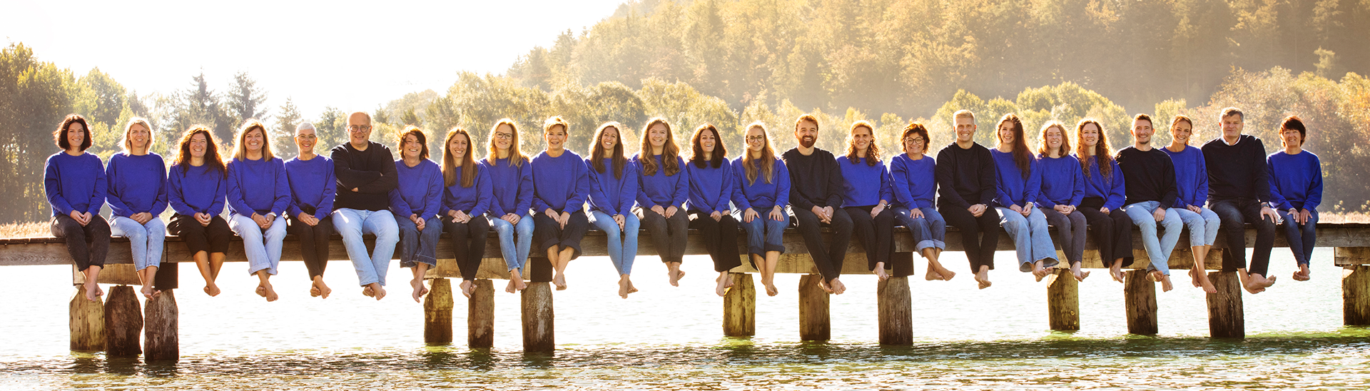Das Team des Achensee Tourismus am Seeufer Das Team des Achensee Tourismus sitzt barfuß auf einem Steg am Ufer des Achensees. Die goldene Herbstsonne taucht die Szenerie in warmes Licht.