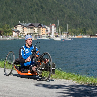 Ein Mann radelt mit seinem Handbike die barrierefreie Route entlang des Achenseeufers in Pertisau.