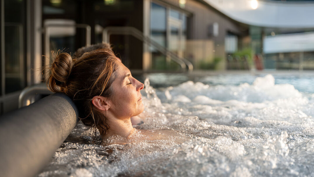 Wellness am Achensee Eine Frau genießt mit geschlossenen Augen den Pool im Wellnessbereich des Atoll Achensee.