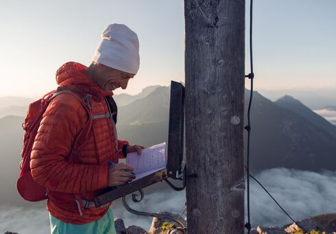 Ein Bergläufer der sich im Gipfelbuch der Seekarspitze im Karwendelgebirge einträgt bei einer schönen Aussicht auf die nebeligen Täler.