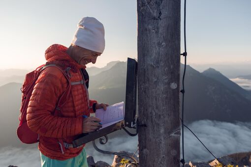Ein Bergläufer der sich im Gipfelbuch der Seekarspitze im Karwendelgebirge einträgt bei einer schönen Aussicht auf die nebeligen Täler.
