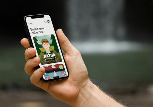 Link öffnen Ein Mann hält sein Handy in der Hand und hat die App der Wunderwege mit dem Achensee Naturerlebnispfad geöffnet.