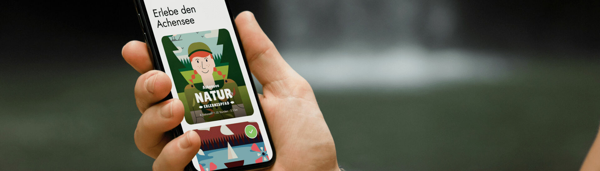 Achensee Natur Erlebnispfad Ein Mann hält sein Handy in der Hand und hat die App der Wunderwege mit dem Achensee Naturerlebnispfad geöffnet.