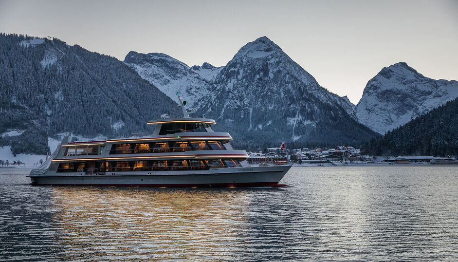 The MS Achensee cruising over Lake Achensee on a winter evening. In the background of this photo is the village of Pertisau and the Karwendel mountains.