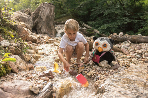 A child splashes around with his owl in the water of a stream.