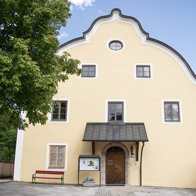 The Notburga museum in Eben The Notburga museum in Eben has several windows and a central entrance door with a canopy. There is an information sign and a bench next to the entrance door.