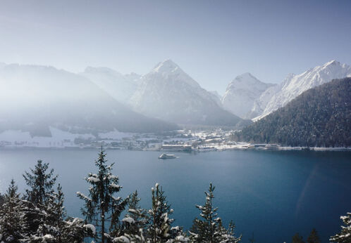 Die Achenseeschifffahrt gleitet über den See. Im Hintergrund das verschneite Pertisau am Achensee.