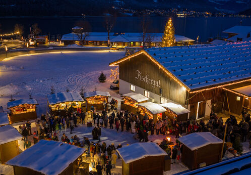 Bergadvent beim Fischergut am Achensee mit weihnachtlich beleuchteten Holzhütten, zahlreichen Besuchern und verschneiter Winterlandschaft am Achensee.